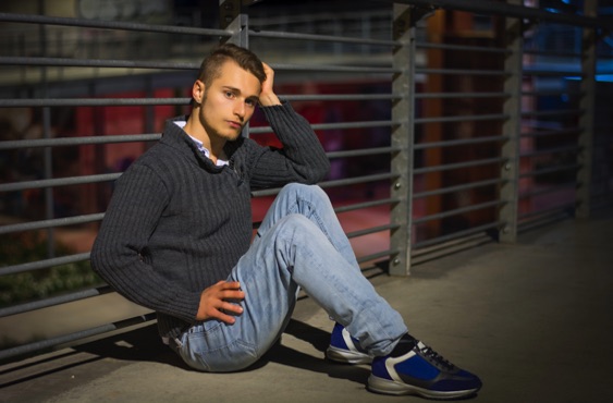 Young man sitting alone in an urban setting at night, reflecting on life after incarceration, prisoner reentry, rehabilitation, second chances, and hope for a successful future.