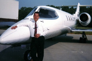 Dave Koch in his pilot uniform leaning on the fron of a Learjet Model 35A
