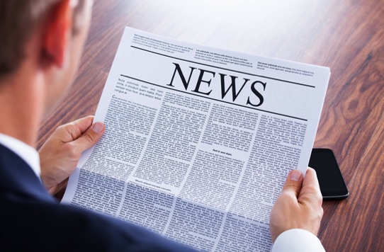 Business executive reading a newspaper representing historic media coverage, business journalism, and press archives documenting Fiber Network Solutions and David J. Koch.
